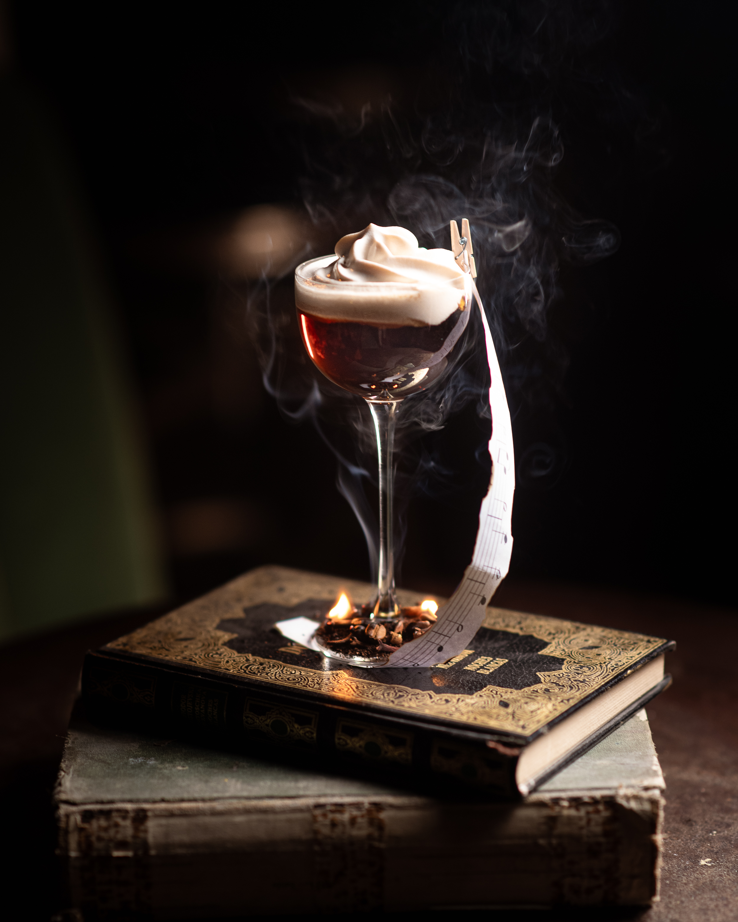 Cóctel de autor Paganini servido sobre libros antiguos con humo, en Enigma Bar