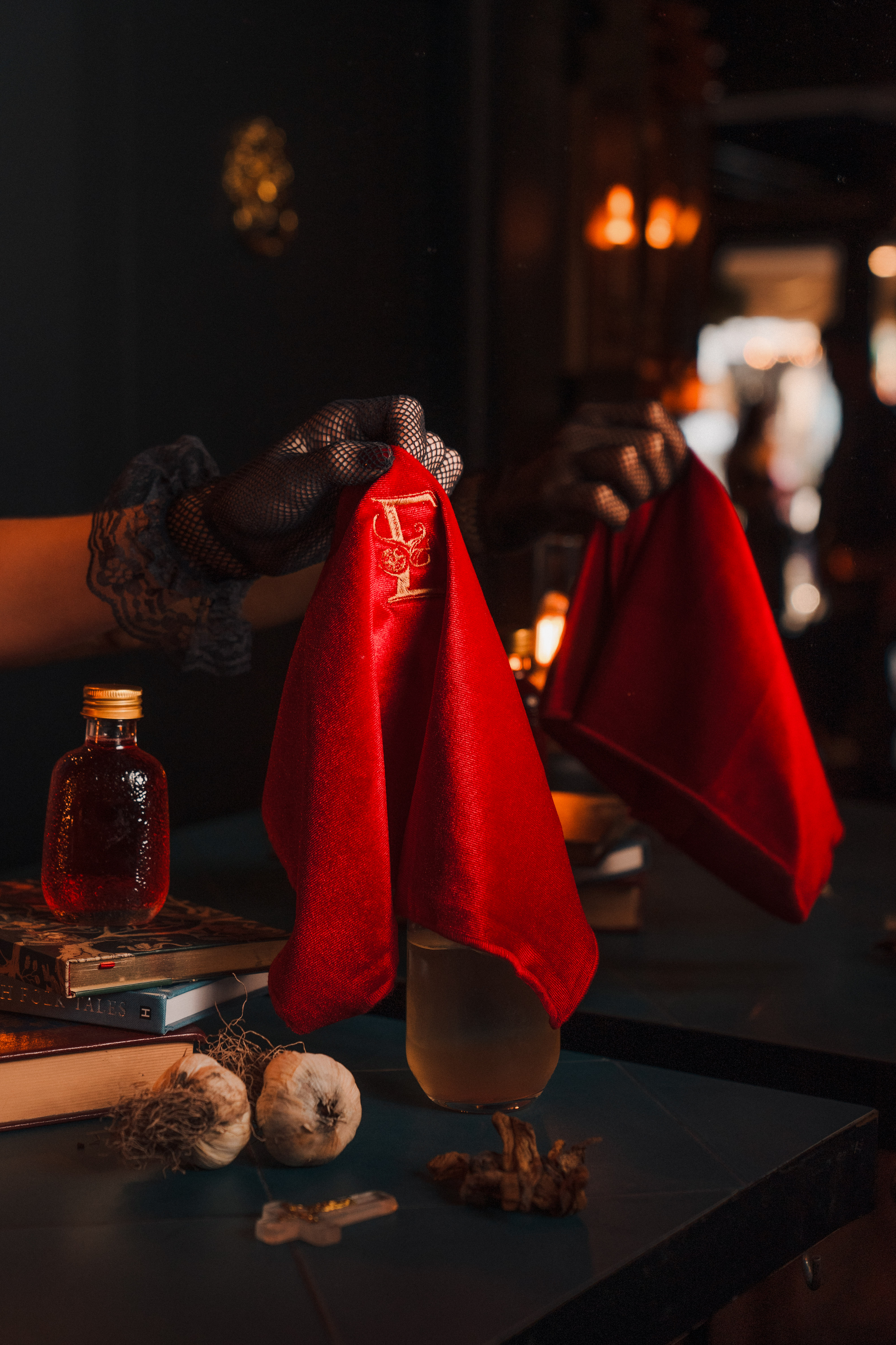 Ritual de coctelería en Enigma: manos con guantes de encaje levantan un paño de terciopelo rojo